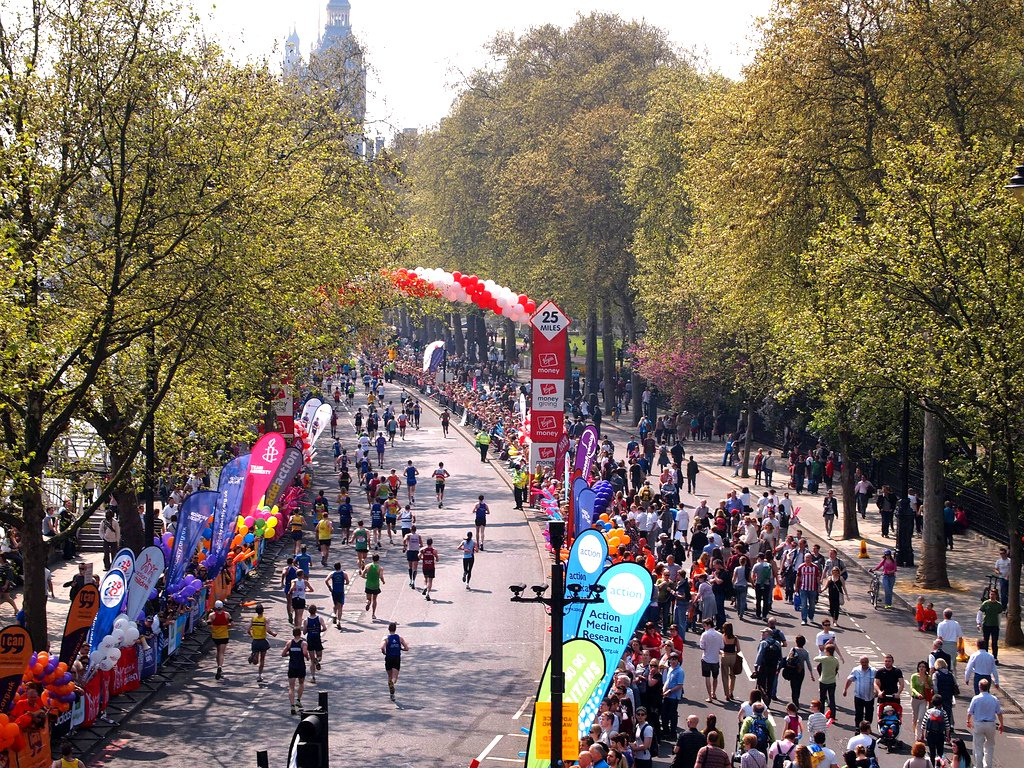 London Marathon runners passing the 25-mile marker on the Embankment, lined with crowds and charity banners